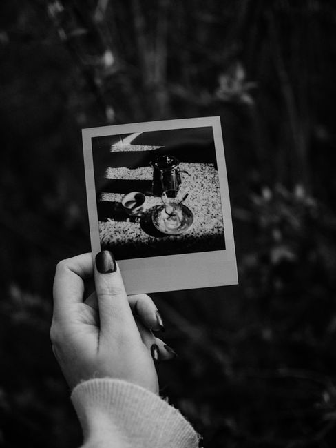 A hand holding a monochrome polaroid picture with blurred outdoor background.