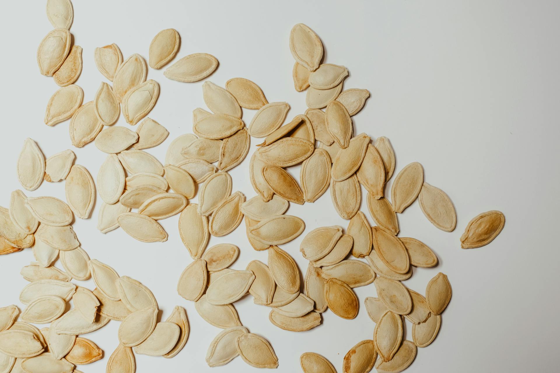 A collection of raw pumpkin seeds scattered on a white surface, perfect for food or health-related content.