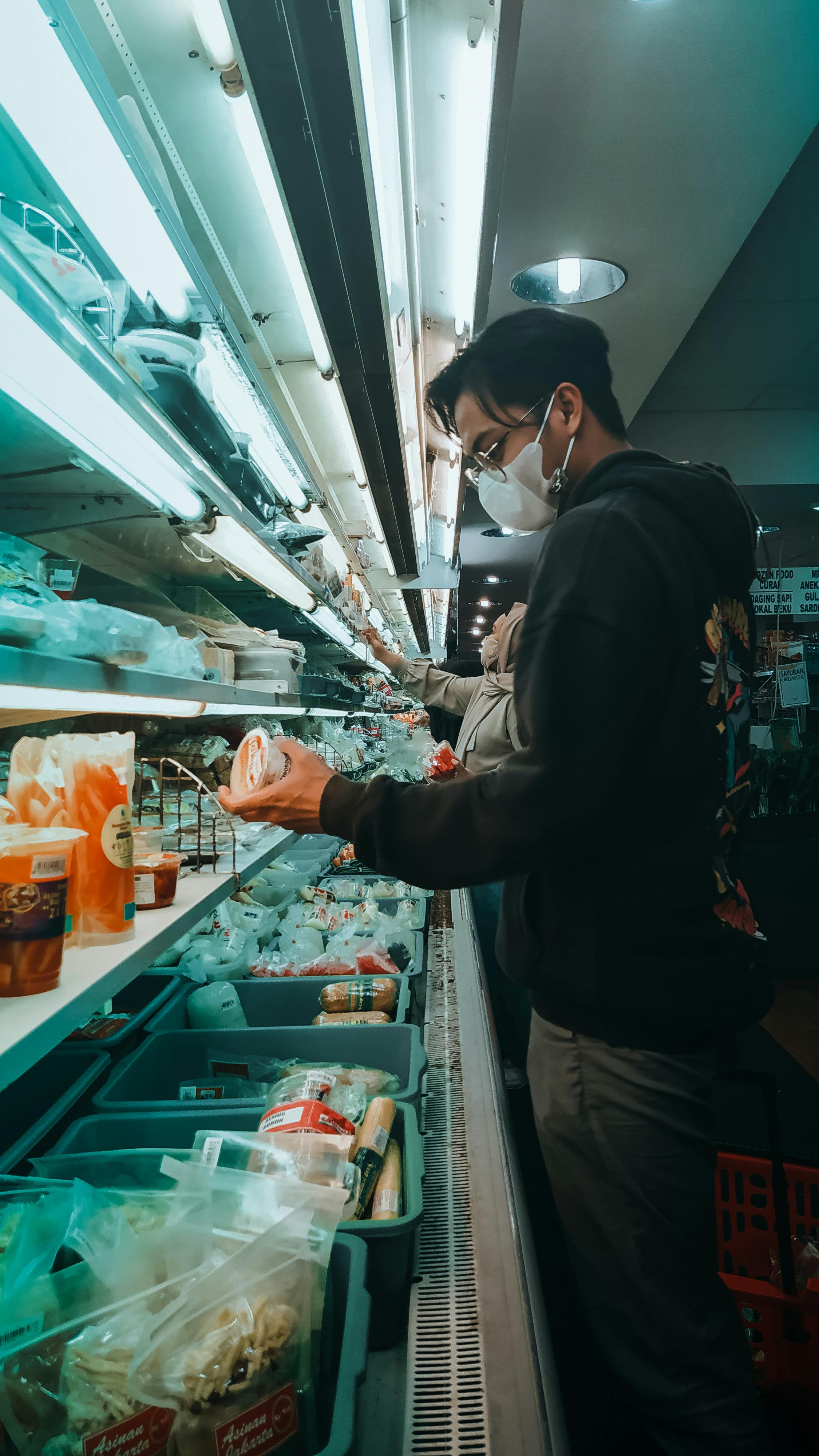 young ethnic man choosing products from fridge in supermarket