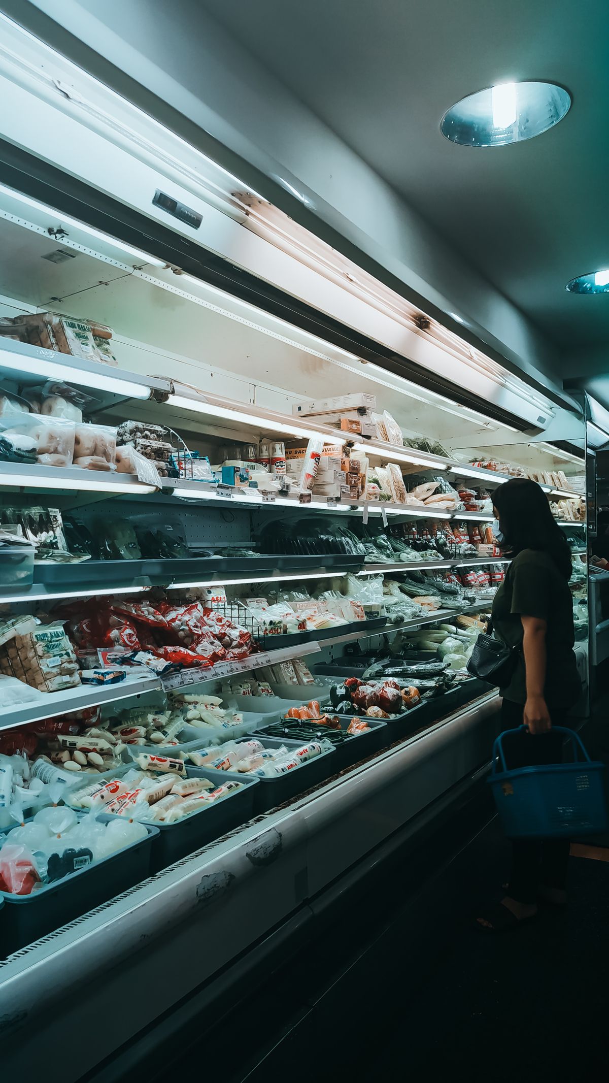 A shopper with a basket choosing products at a chilled supermarket display