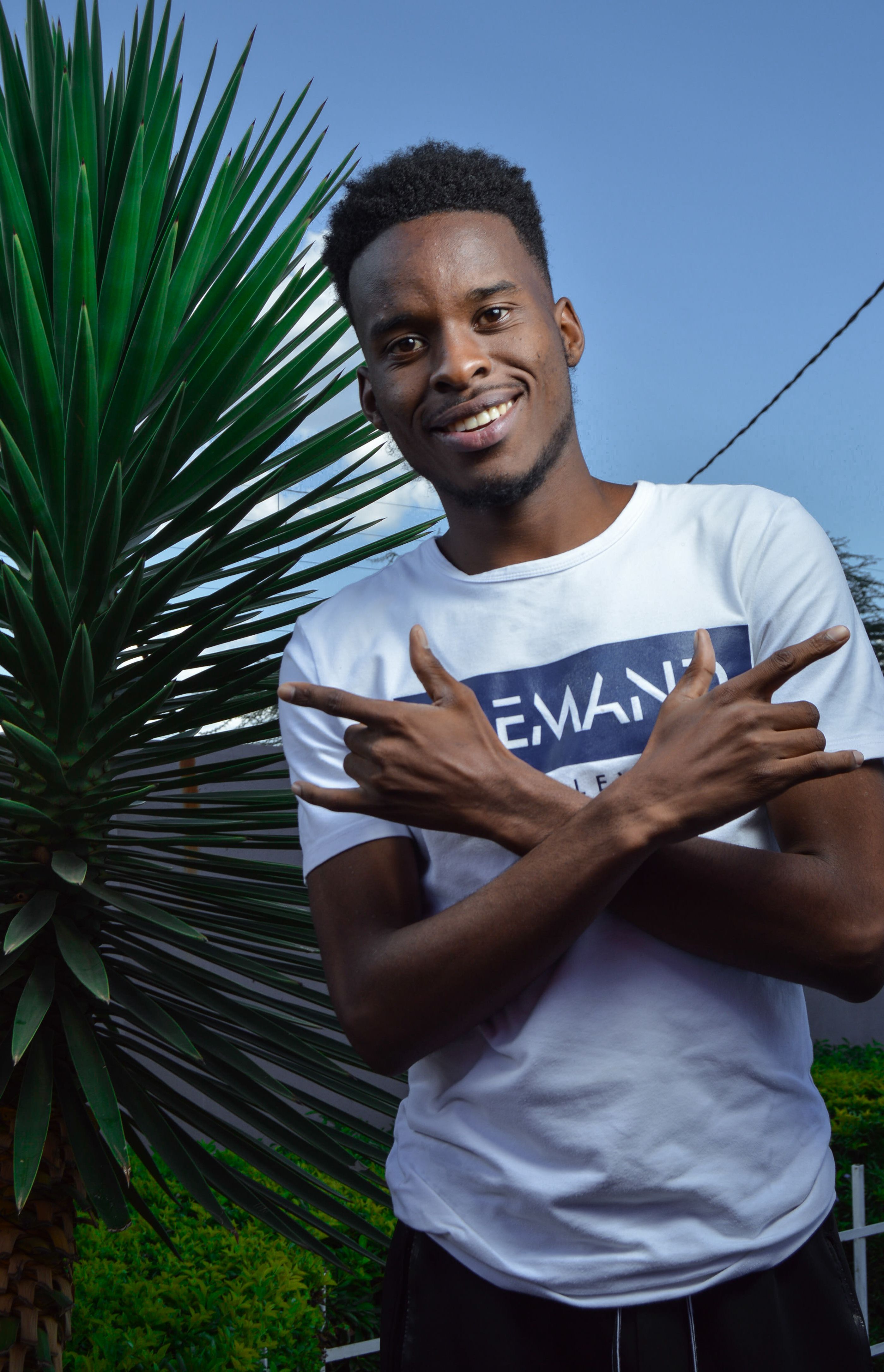 A joyful man in a white t-shirt poses outdoors with a plant backdrop, exuding energy.