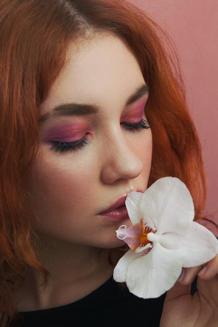 Thoughtful Woman In Makeup With Blooming Flower In Studio