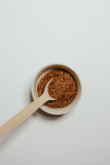 A small glass bowl of thick, gel-like flax egg made from ground flaxseed and water, with a spoon of whole flaxseeds beside it.