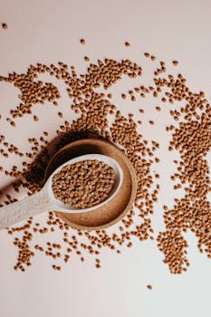 A high-angle shot of scattered buckwheat on a white surface with a wooden spoon and plate.