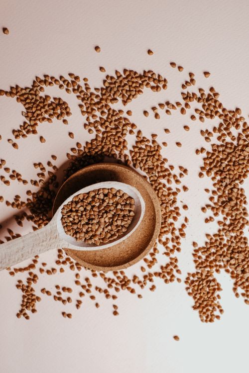 Free A high-angle shot of scattered buckwheat on a white surface with a wooden spoon and plate. Stock Photo