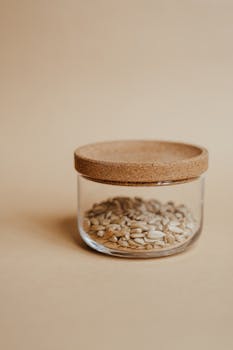 A glass jar filled with sunflower seeds, placed on a beige surface, creating a warm and minimalistic look.
