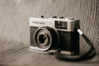 Aged compact photo camera with lens under inscription and numbers on metal surface on blurred background