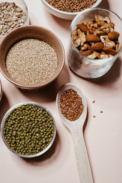 Flatlay de amêndoas, sementes, lentilhas, quinoa e nozes em tigelas de porcelana sobre superfície de madeira