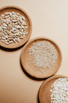 Top view of assorted seeds and grains in rustic bowls on a neutral background, ideal for healthy eating concepts.