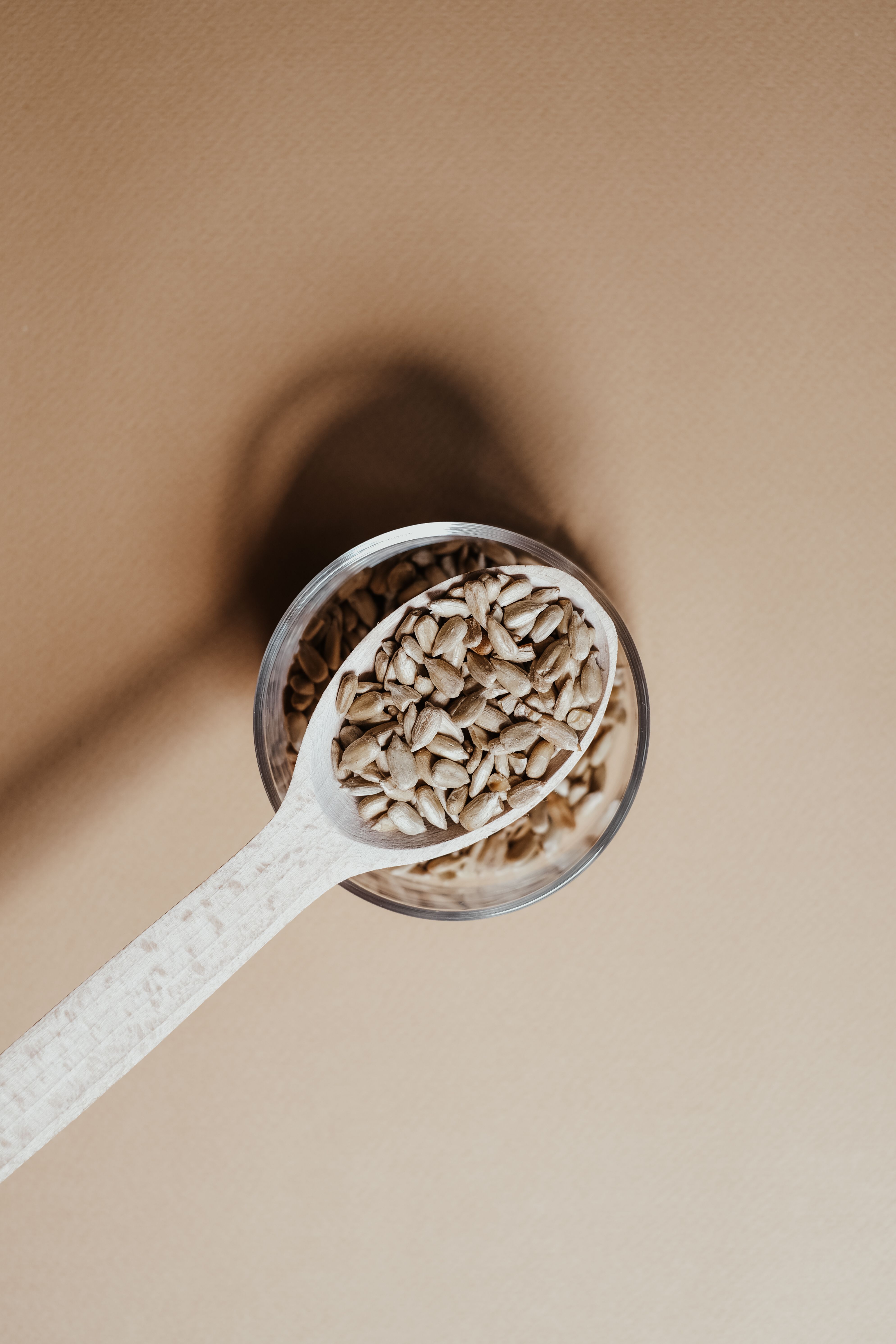 Wooden spoon filled with natural seeds on a light brown surface, highlighting organic simplicity.