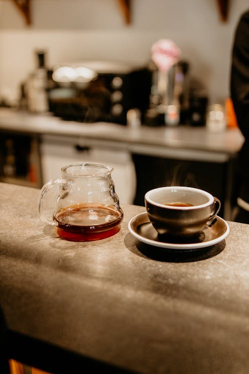 Mug of freshly brewed aromatic coffee near glass pot placed on counter in cafe with modern appliances on blurred background