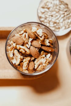 A high-angle shot of almonds and walnuts in a glass bowl on a wooden tray.