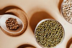 Top view of assorted grains and seeds including mung beans, buckwheat, and rice on a beige surface.