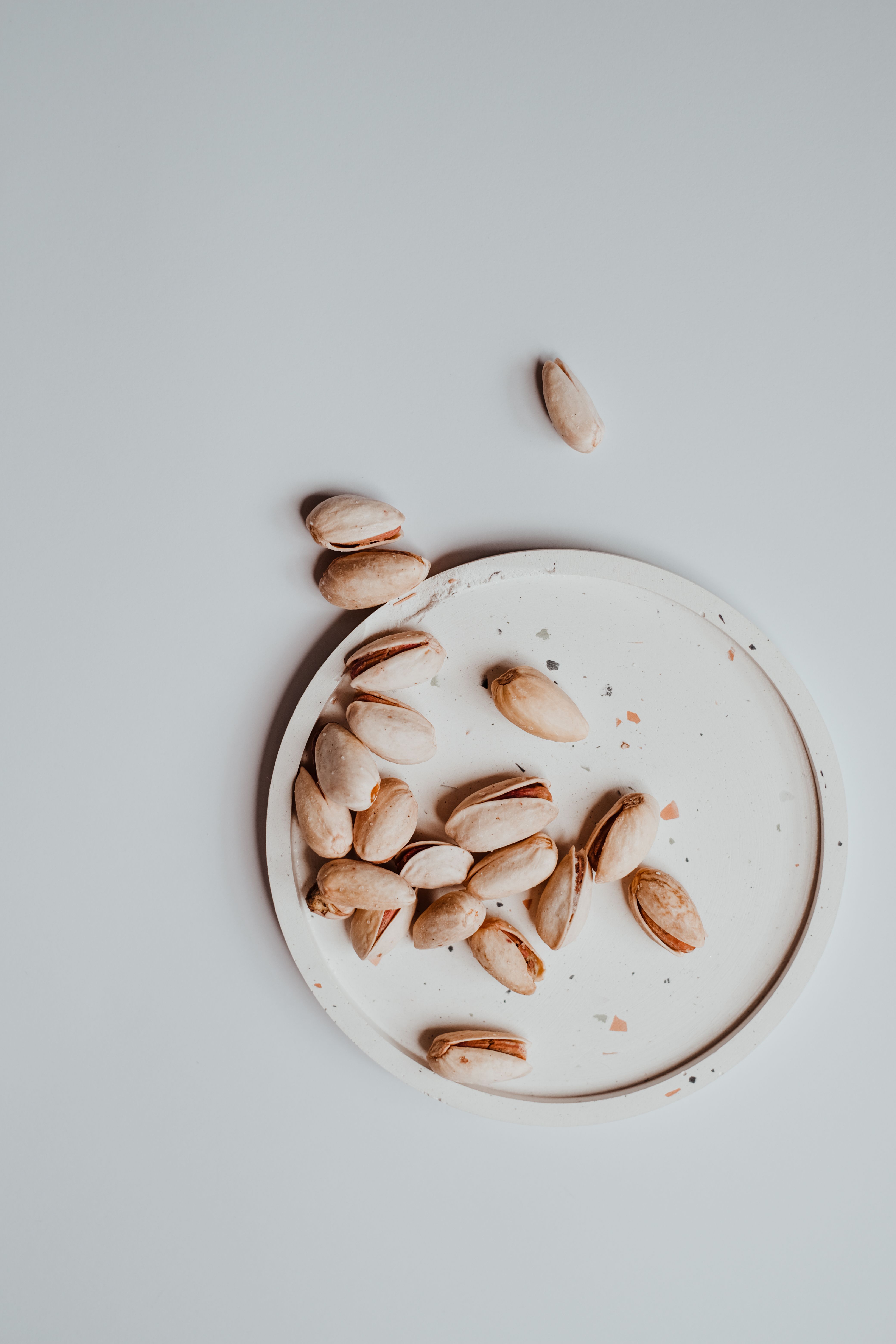 Overhead view of pistachios on a saucer against a neutral background.