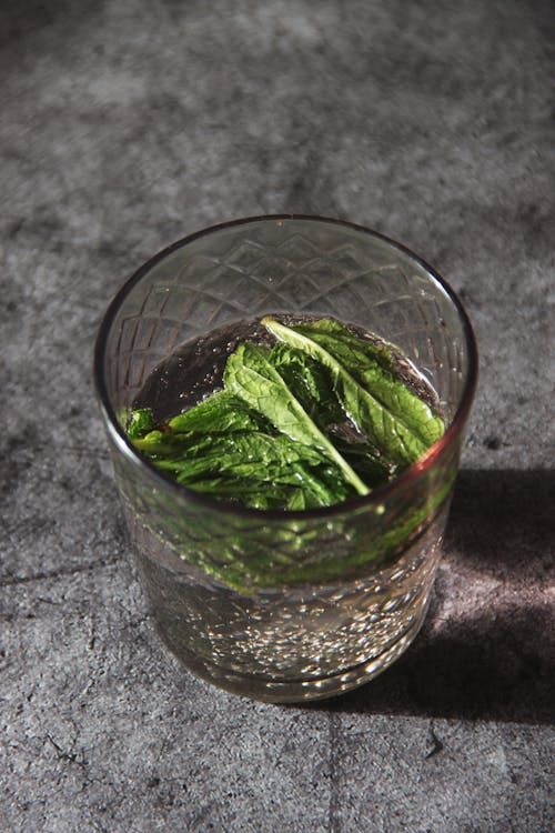 From above of glass cup of refreshing water with sorrel leaves placed on gray table