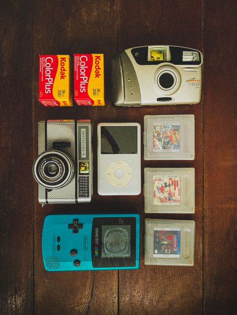 Flat lay of vintage electronics and gadgets including cameras, iPod, and Game Boy on a wooden table.