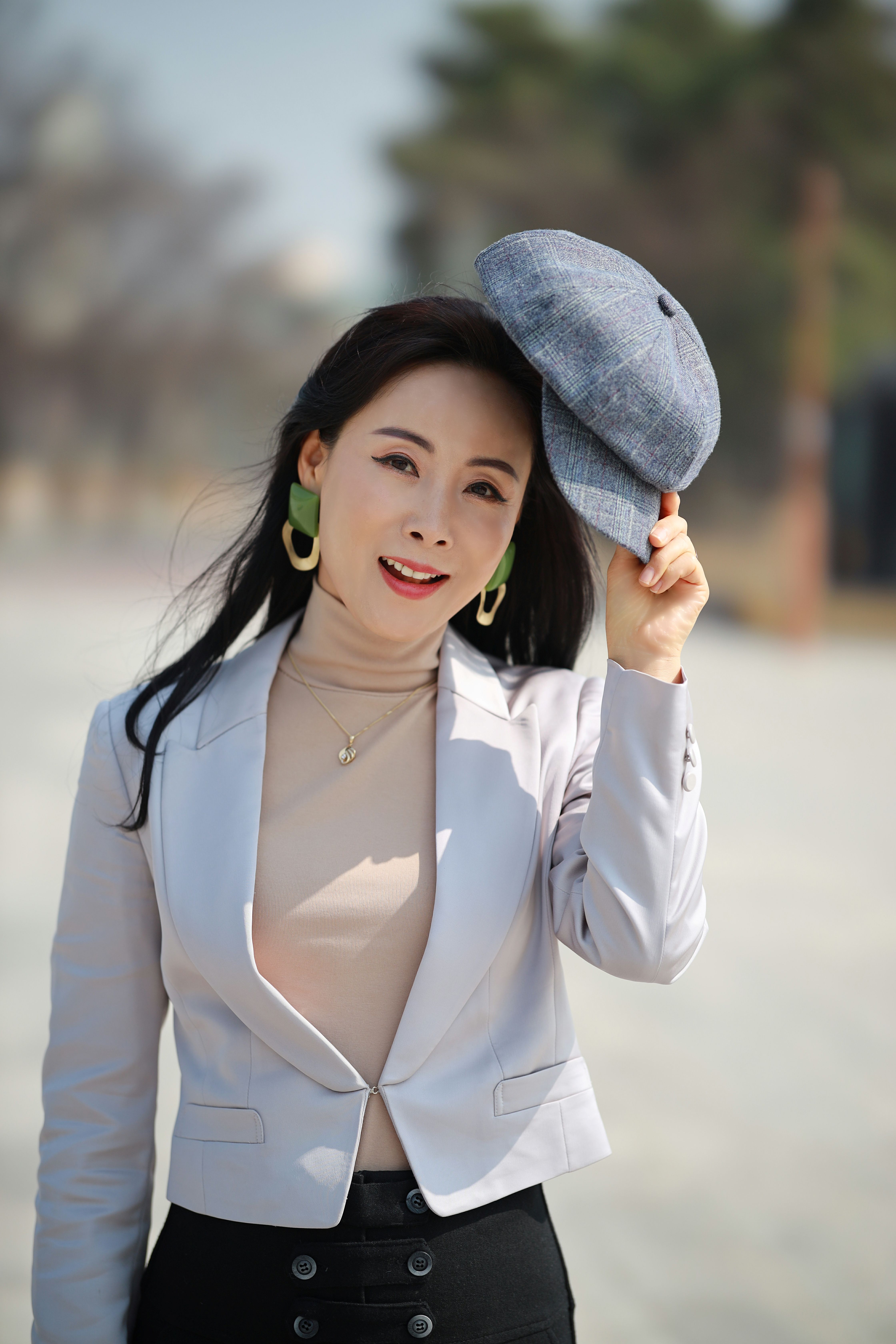 Beautiful Asian woman in a white blazer and hat enjoying an outdoor day.