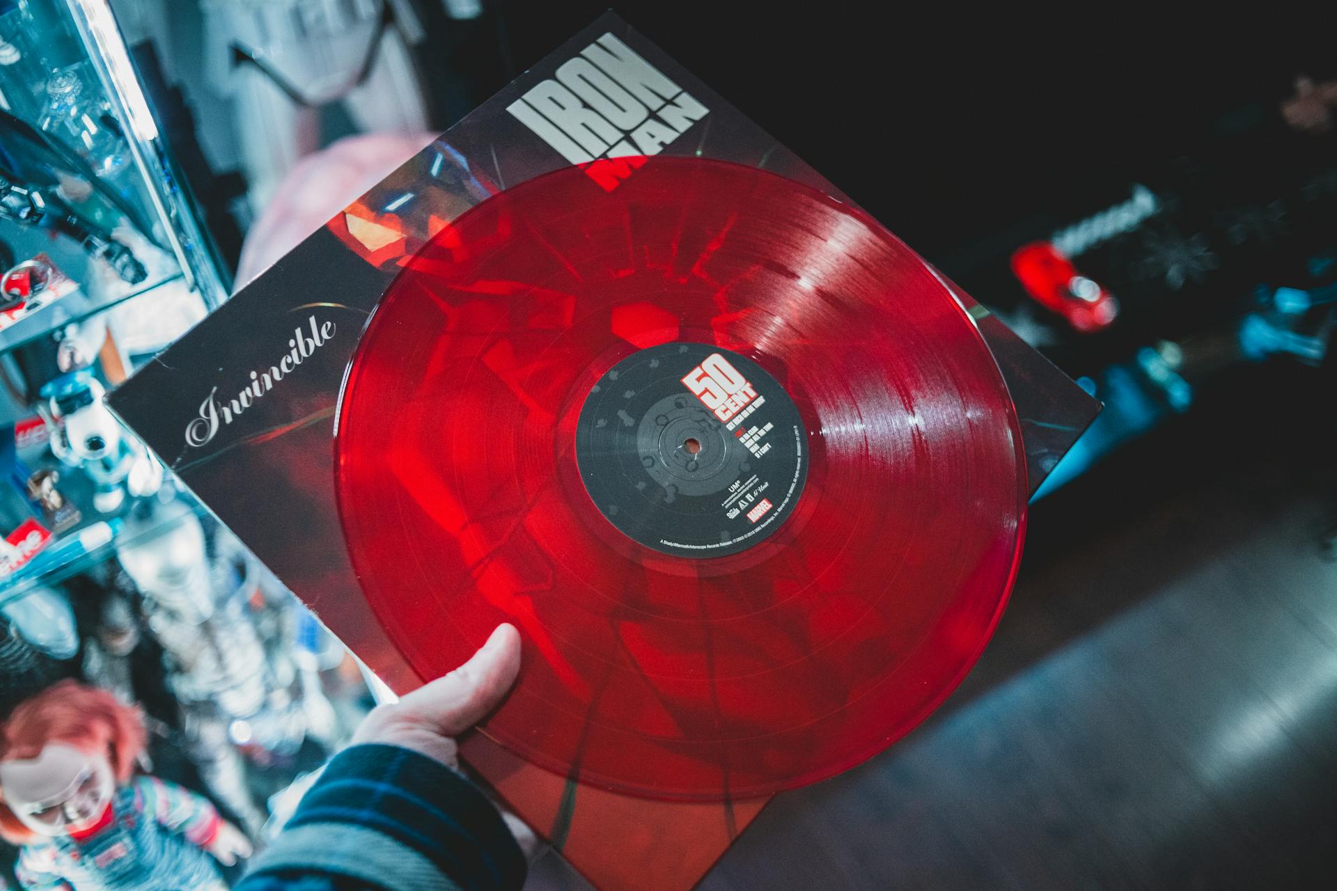 From above crop person holding red vinyl disc with inscription cover in music shop