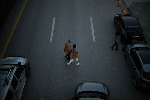 Free Two adults crossing a city road with parked cars on each side from a high angle. Stock Photo