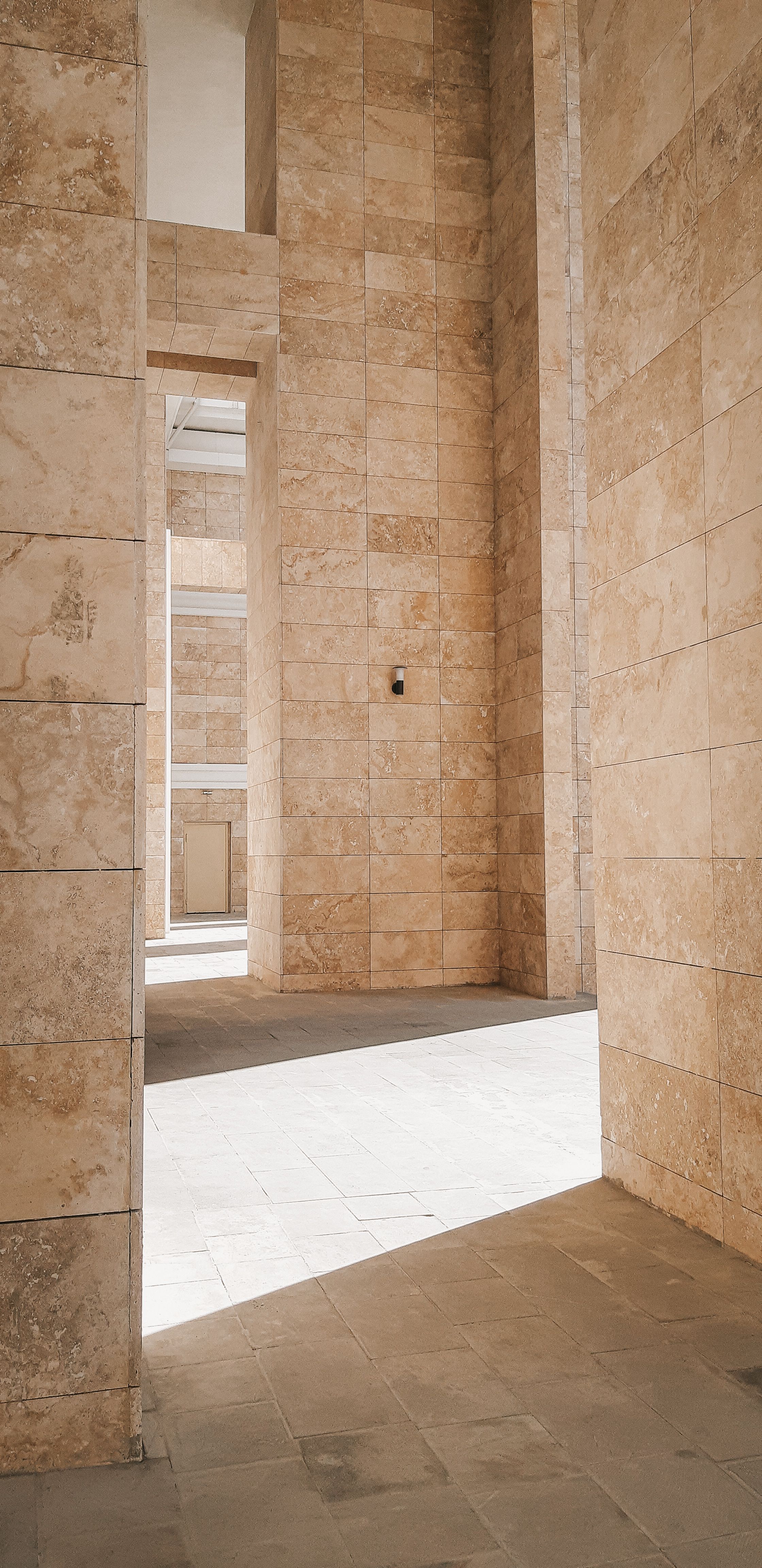 Sunlit stone corridor showcasing elegant architectural design with tall walls and shadows.