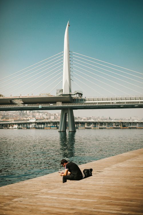 Free A lone man sits on a dock, with a metro bridge over water in Istanbul. Stock Photo