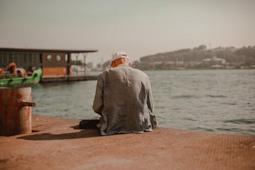 Man in Gray Robe Sitting on Brown Concrete Dock