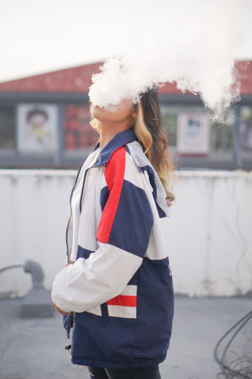 Free A stylish woman in a colorful jacket exhaling smoke in an outdoor setting. Stock Photo