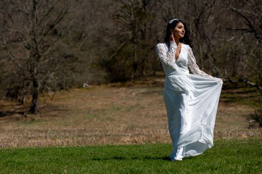 A beautiful woman in a bridal gown poses outdoors in a sunlit field during the day, showcasing elegance and grace.