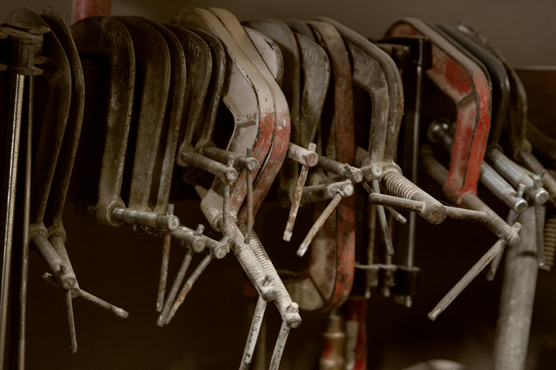 Set of weathered rusty metal clamps hanging on rack in grungy carpentry workshop