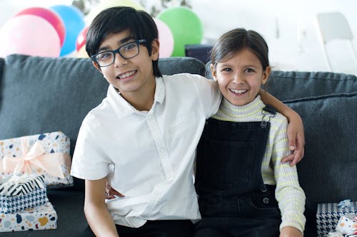 A Young Girl and Boy Smiling while Sitting on the Couch