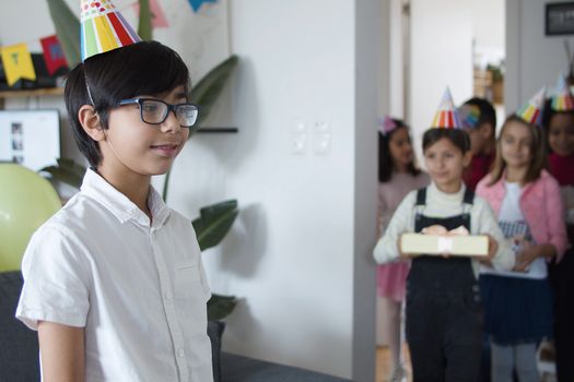 Children celebrating a birthday party indoors with gifts and party hats.