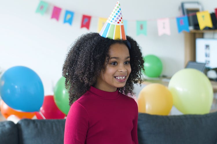 Girl In Red Long Sleeve Shirt Smiling And Wearing Birthday Cone Hat