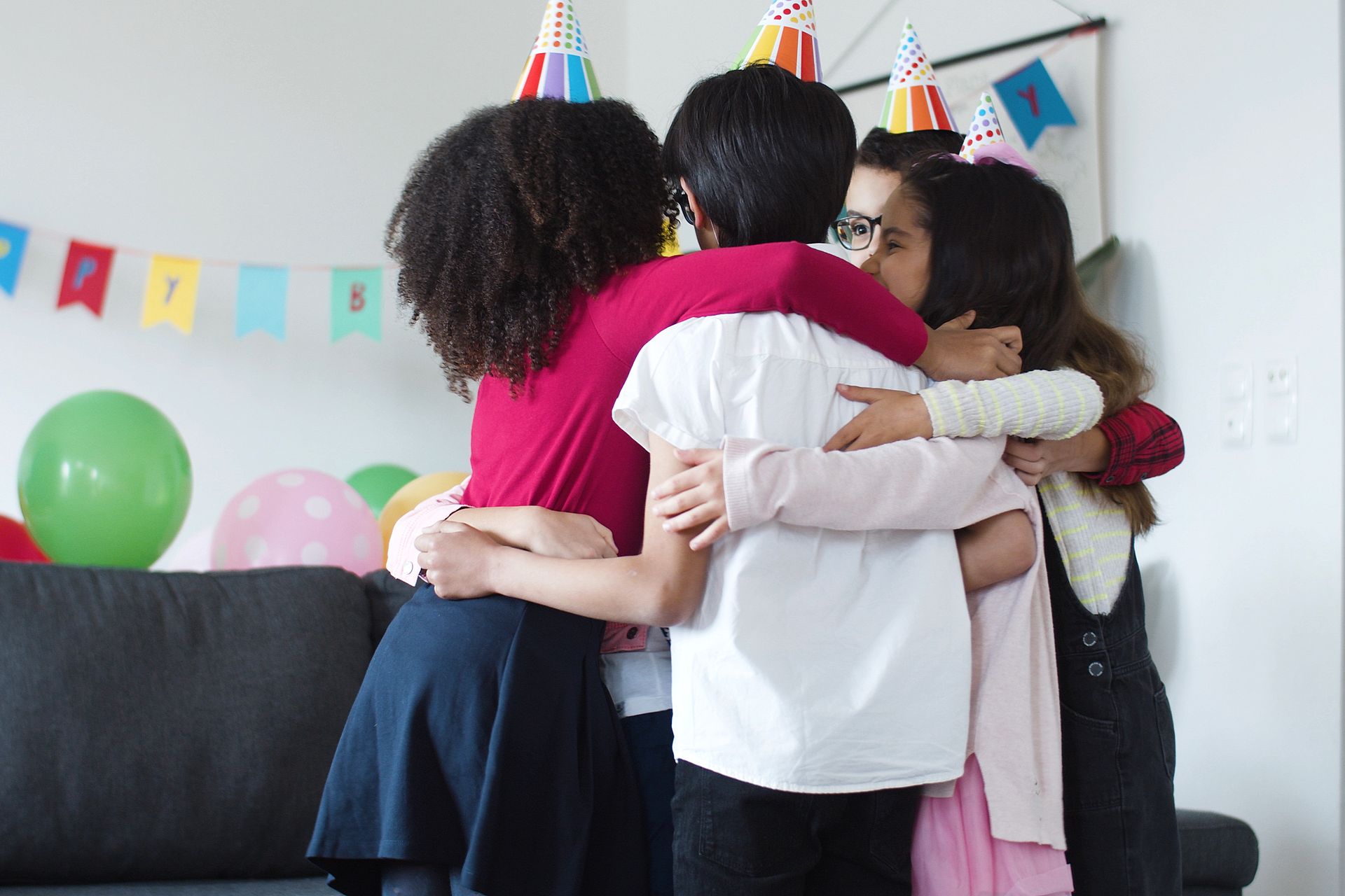 A group of children joyfully embraces at a colorful birthday party indoors.