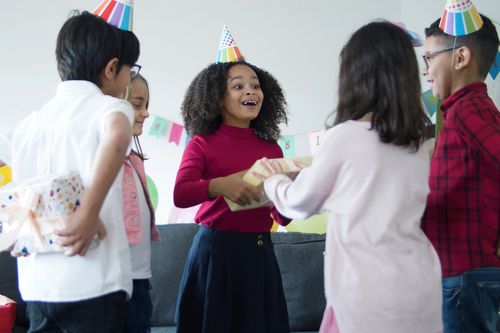 Free Children celebrating a birthday party indoors, joyfully sharing gifts and wearing party hats. Stock Photo