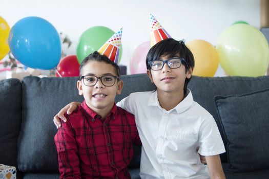Two boys celebrating a birthday with party hats and balloons indoors.