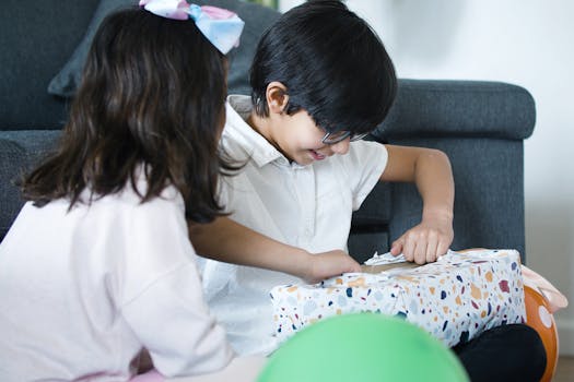 Two happy children unwrapping gifts, captured indoors during a joyful birthday celebration.