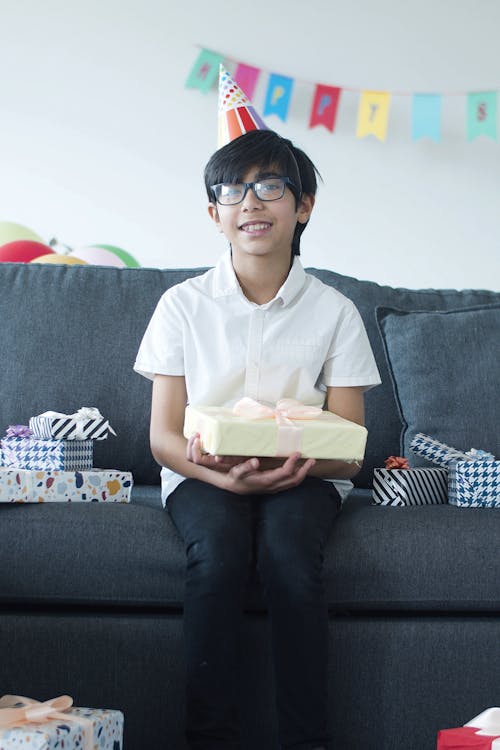 Free A Young Boy Wearing a Party Hat while Sitting on the Couch Stock Photo