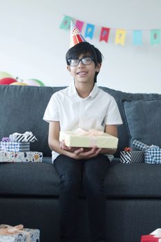 A cheerful boy in a party hat holds a present during a vibrant birthday celebration at home.