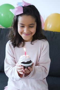 A cheerful girl holding a cupcake with a lit candle, celebrating indoors.