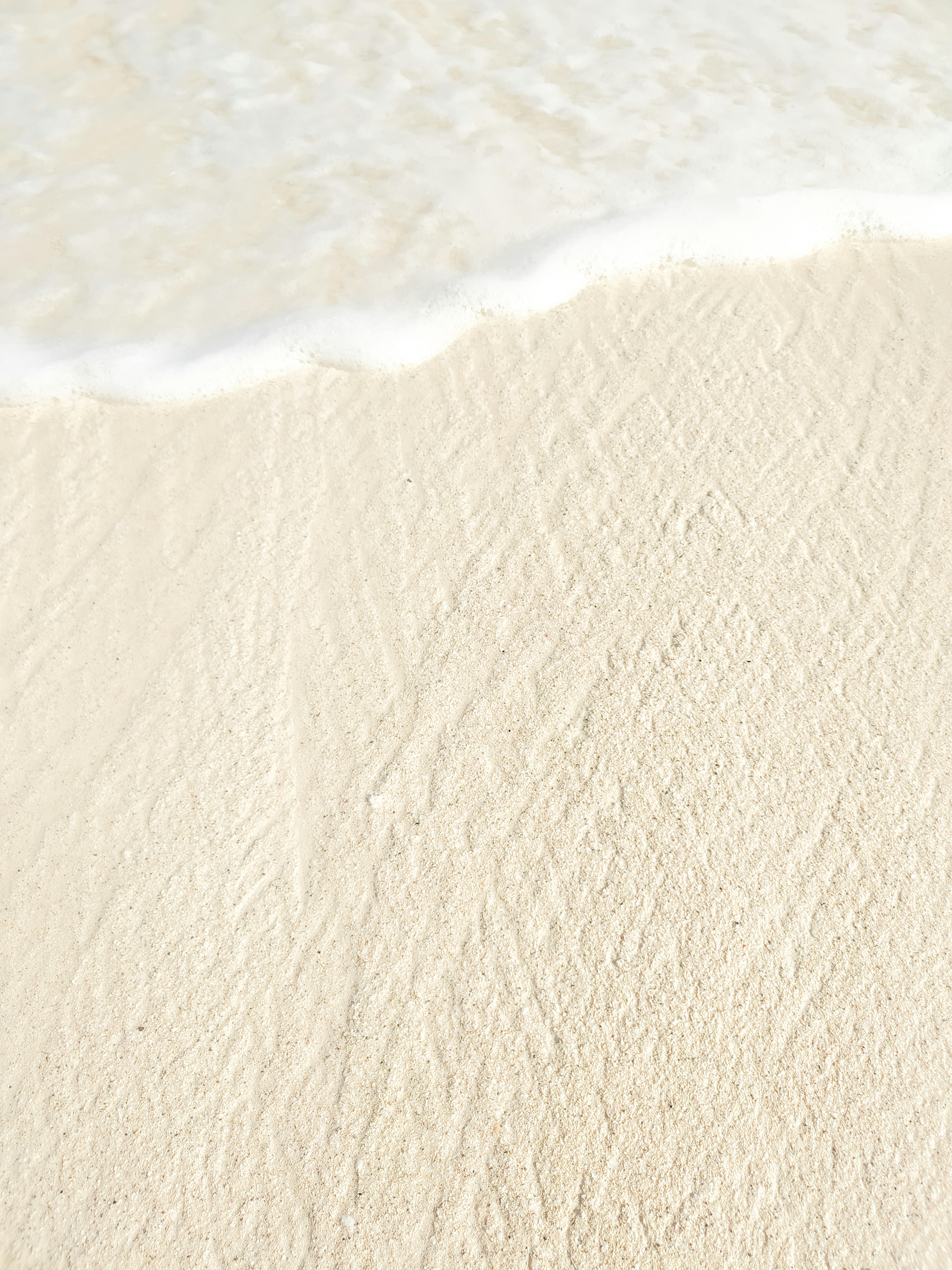 Peaceful white sand and gentle sea foam meet in Cancún, capturing serene coastal beauty.