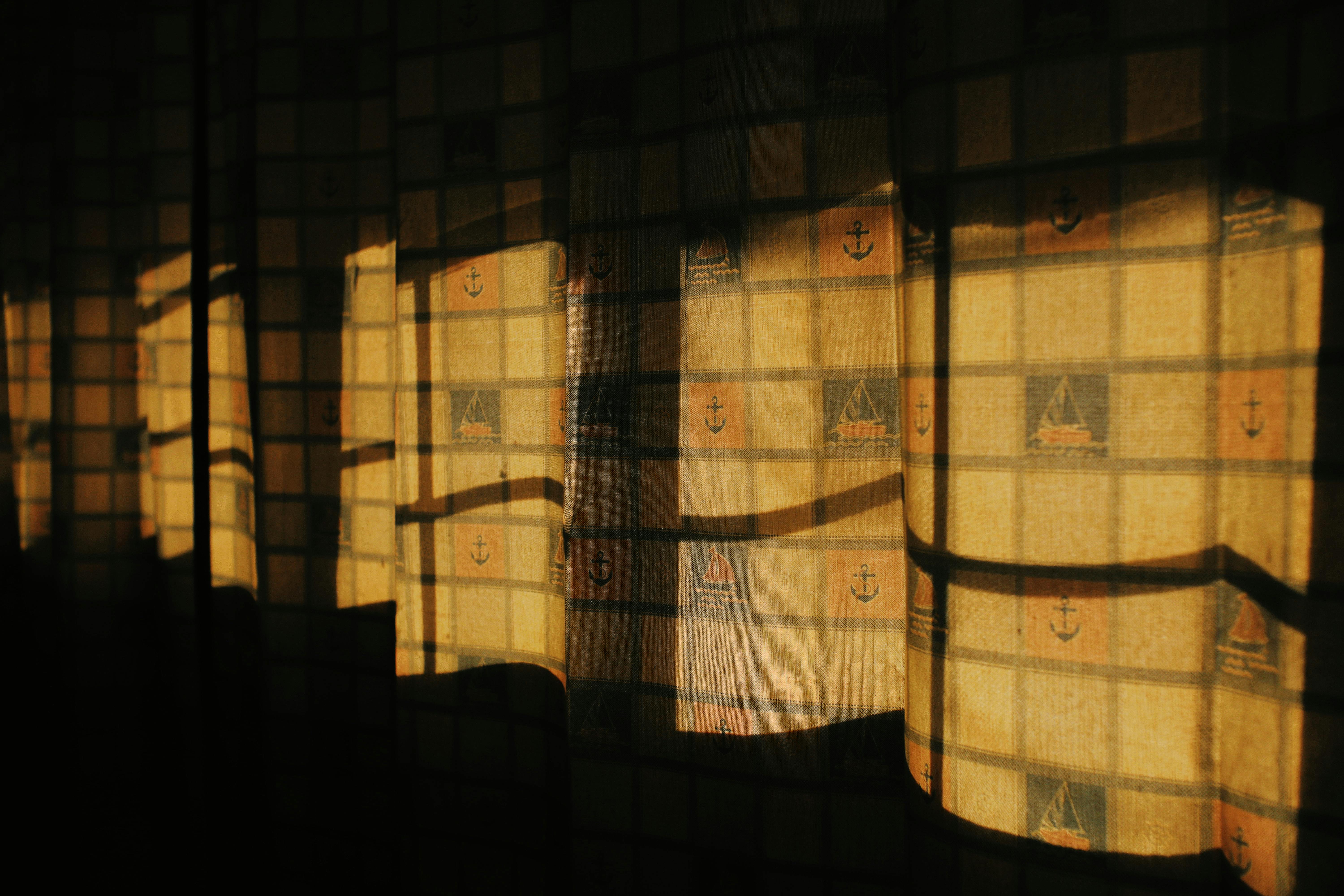 Colorful yellow curtains with creative nautical style and shadows of window hanging in dark room with dim light at home