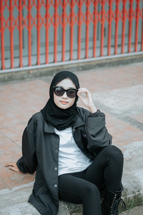 A Woman in Black Hijab and Sunglasses Sitting on the Street