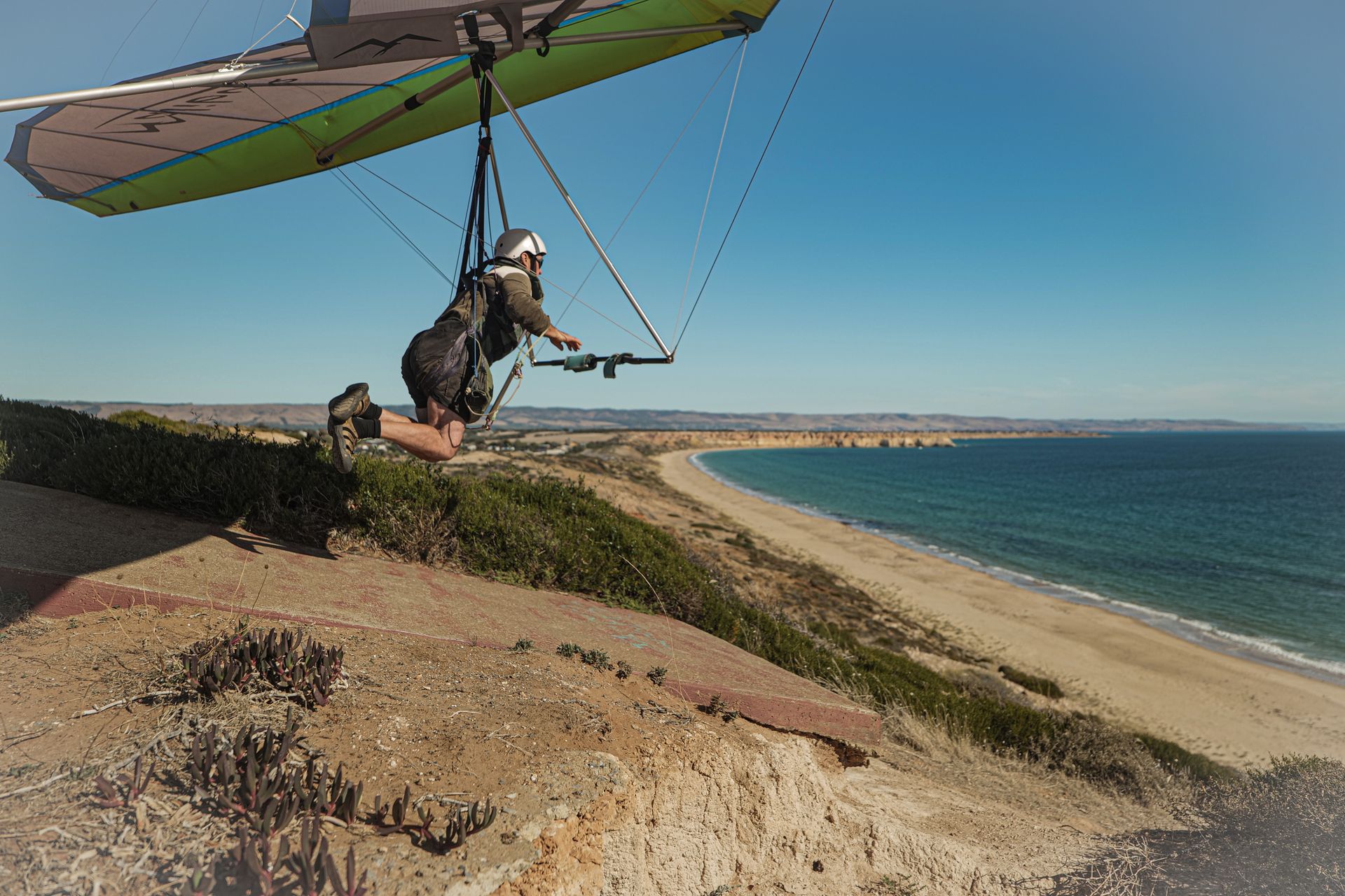 A hang glider pilot launching off a coastal cliff, enjoying a thrilling adventure sport by the ocean.