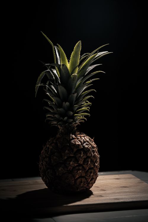 Free Moody studio image of a fresh pineapple on a wooden chopping board, highlighting its texture and freshness. Stock Photo