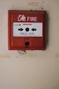 Manual emergency red fire alarm system box with push button placed on white shabby wall in light room of building