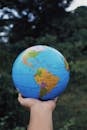 Crop anonymous person reaching out hand and showing Earth globe against green plants in daytime