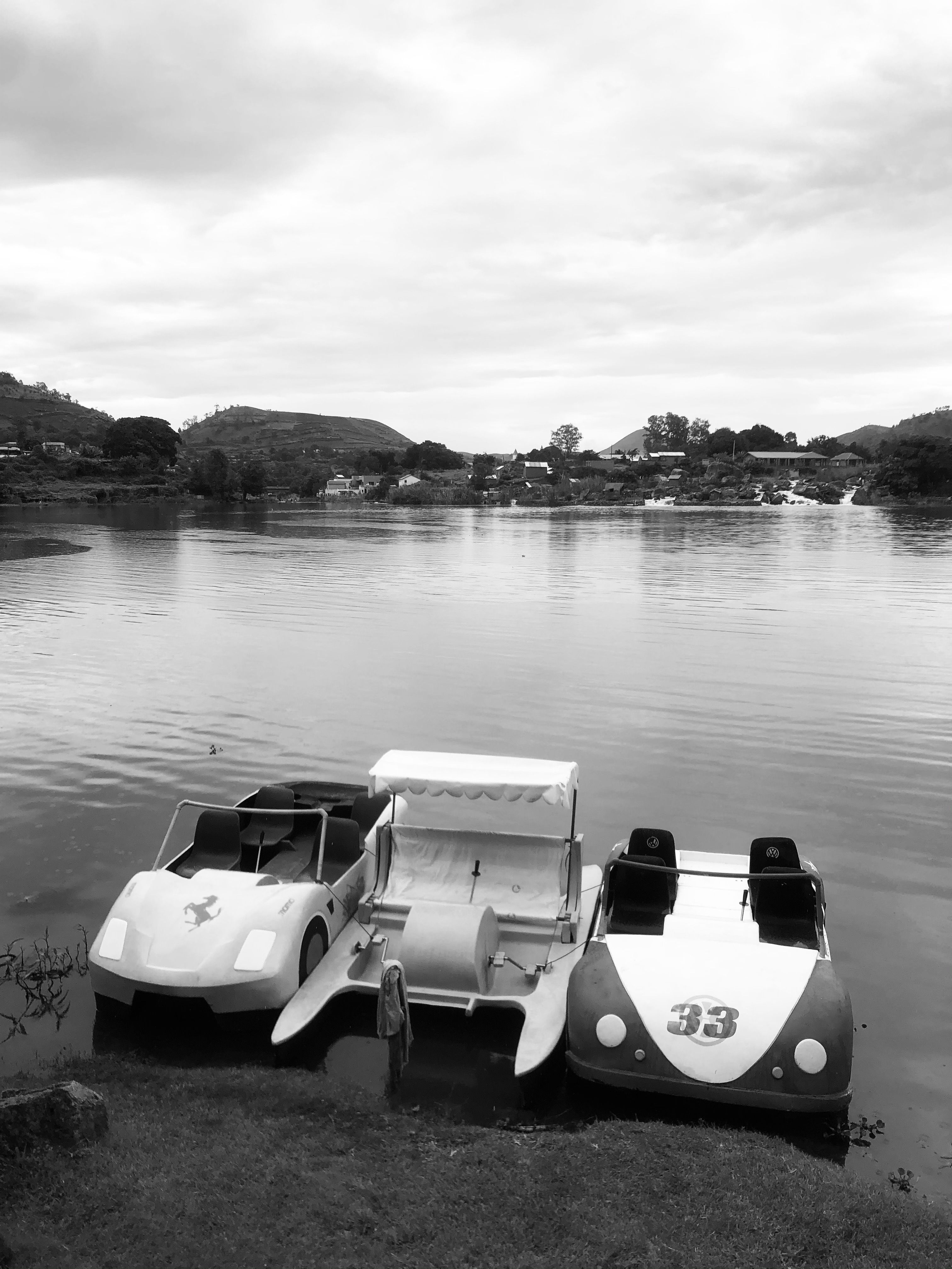 Three pedal boats moored by the tranquil lake shore in black and white, showcasing Antananarivo's scenic beauty.