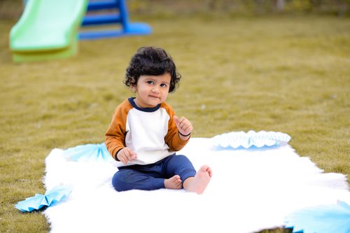 Free A cute child sitting on a mat in a sunny park with toys around, perfect capture of innocence. Stock Photo