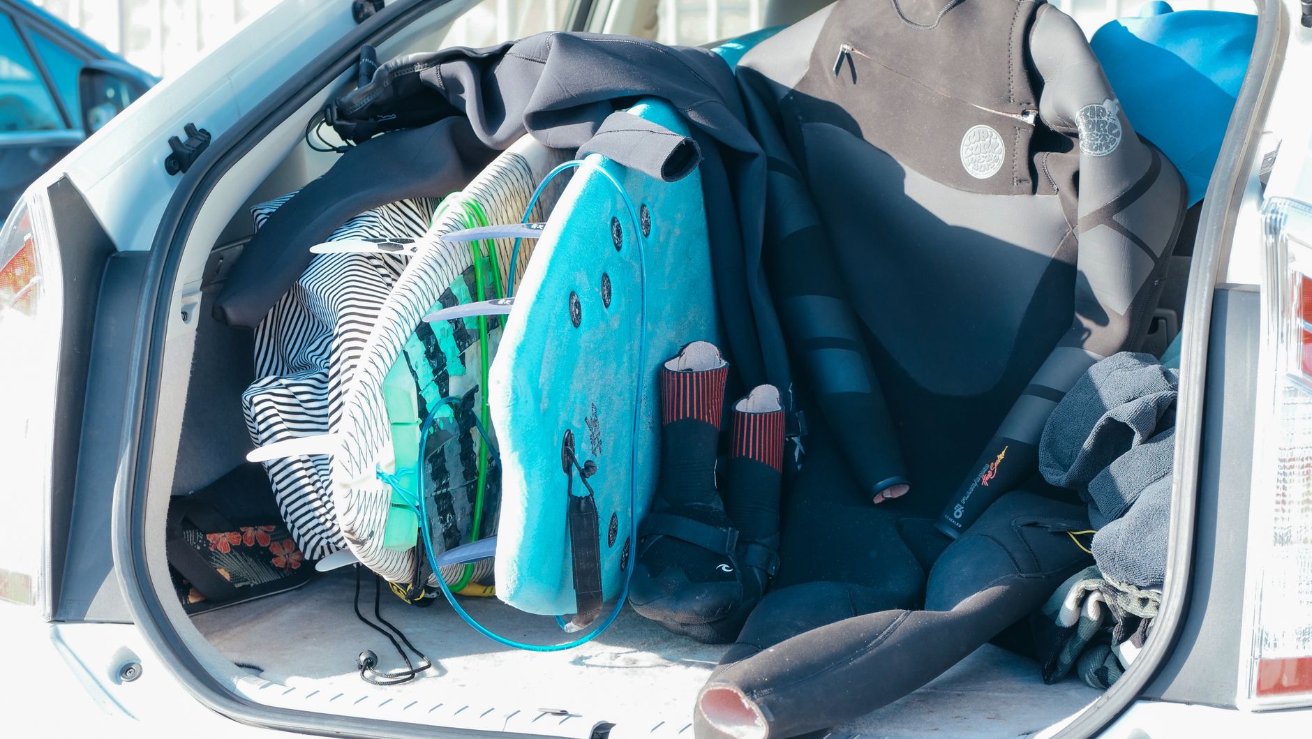 Maletero de coche cargado con tablas de surf y trajes de neopreno, listo para la aventura en la playa.