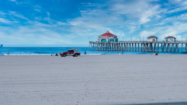 Serene view of Huntington Beach Pier with lifeguard vehicle and visitors enjoying the sunny coastline.